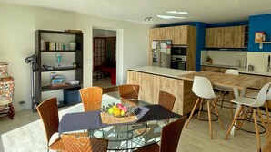 A modern kitchen with wooden cabinets, a central island, and a dining area with a glass table and wicker chairs. - Beautiful villa with mountain view, Beautiful villa with mountain view (Châteauneuf)