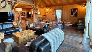 A rustic wooden interior with leather sofas, a wooden coffee table, and a dining area with chairs. - Luxurious 5 bedroom chalet, Luxurious 5 bedroom chalet (Brizon)
