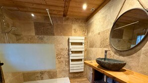 A bathroom with a stone sink, a round mirror, and a white towel rack.