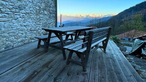 A wooden picnic table and bench on a wooden deck with a stone wall backdrop and a mountain view. - Luxurious 5 bedroom chalet, Luxurious 5 bedroom chalet (Brizon)