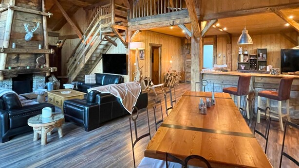 A rustic cabin interior with a wooden dining table, leather sofas, a fireplace, and a staircase. - Luxurious 5 bedroom chalet, Luxurious 5 bedroom chalet (Brizon)