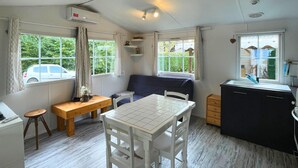 A compact kitchen with a dining table, a bench, and a sofa. There are windows with curtains, a small stool, and a cabinet. - Spacious mobile home + terrace !, Spacious mobile home + terrace ! (Verchaix)
