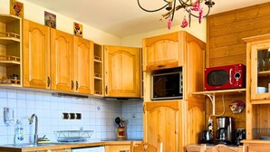 Een houten keuken met een eettafel en stoelen, een magnetron, en diverse keukenapparaten.