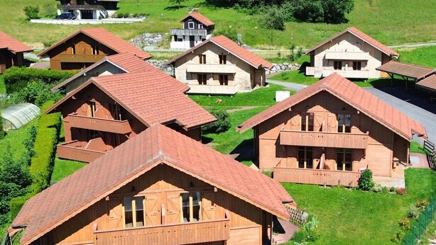 Een groepje houten vakantiehuisjes met puntige daken, omgeven door weelderige groene velden en bomen.
