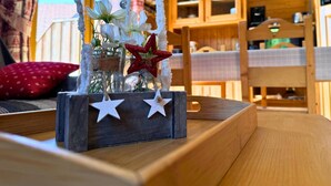 Une table en bois rustique, agrémentée d’un centre de table décoratif composé de fleurs blanches et d’étoiles rouges, placée devant une fenêtre ornée de rideaux.