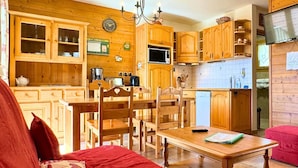 Une cuisine chaleureuse avec des meubles en bois, une table à manger et des chaises. Il y a une horloge au mur et un téléviseur sur le côté droit.