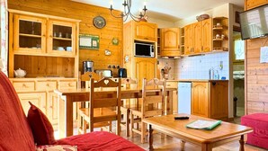 A cozy kitchen with wooden cabinets, a dining table, and chairs. There is a clock on the wall and a television on the right. - Z-Chalet Mitoyen 2B., Z-Chalet Mitoyen 2B. (Mont-Saxonnex)