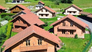 Un ensemble de chalets en bois aux toits en pente, entourés de prairies verdoyantes et d’arbres.