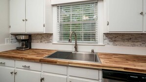 Una cocina con gabinetes blancos, encimera de madera, pileta de acero inoxidable y cafetera.