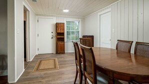 Un comedor con una amplia mesa de madera, seis sillas, un armario de madera y una ventana con persianas.