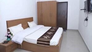 A bedroom with a wooden bed, white bedding, a nightstand with a vase of flowers, and a wardrobe. - Shree Jee Dham (Mathura)