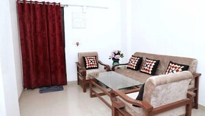 A living room with a sofa, two armchairs, a coffee table, and a red curtain. - Shree Jee Dham (Mathura)