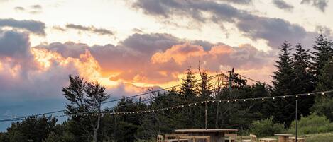 A rustic outdoor setting with wooden furniture and string lights against a sunset sky.