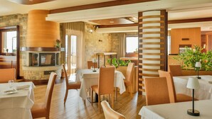 A restaurant with wooden flooring, white tablecloths, and orange chairs. There is a stone wall and a fireplace. - Hotel Monte Campo Ristorante Santa Lucia (Capracotta)