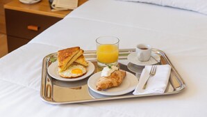 A neatly made bed with white linens, a tray with breakfast including toast, eggs, juice, and a croissant, and a nightstand with a vase of flowers and a coffee pot. - Hotel Monte Campo Ristorante Santa Lucia (Capracotta)