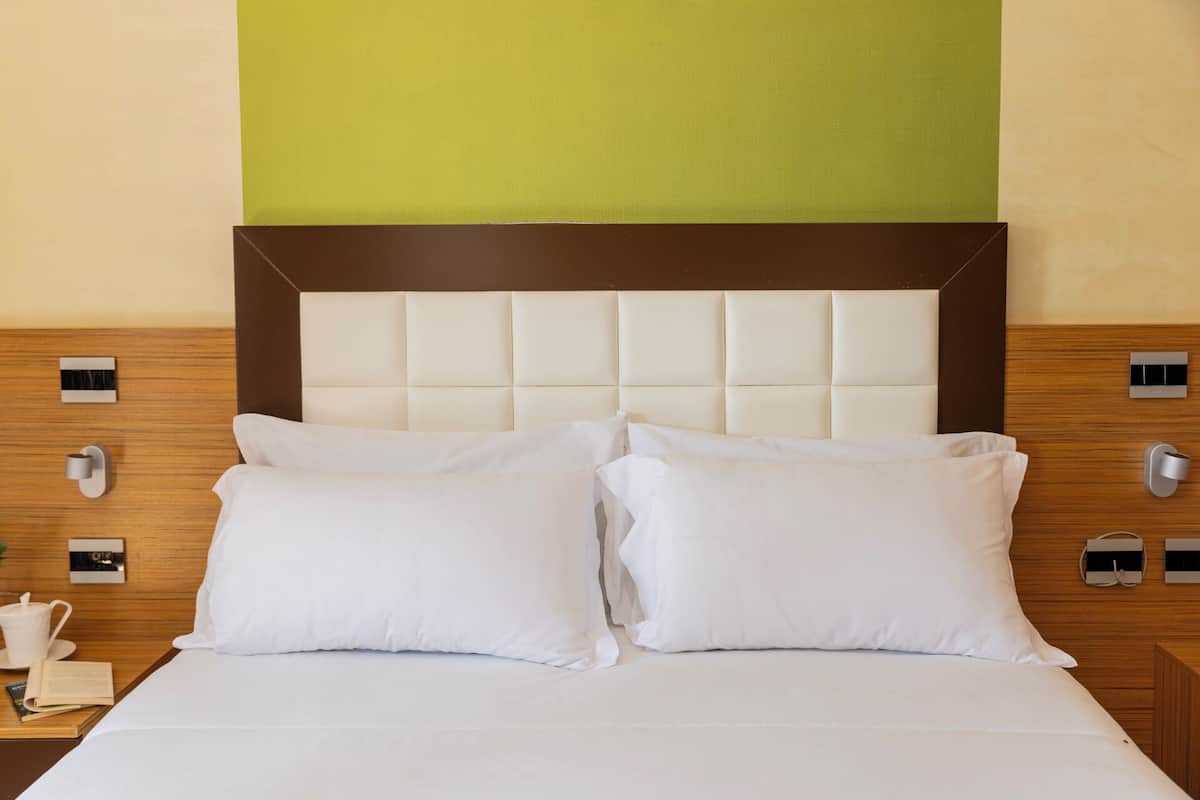 Habitación de hotel con una cama grande, dos almohadas, cabecero de madera y una pared de acento verde.
