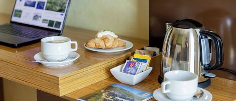 A wooden reception desk with a laptop, a cup of coffee, a croissant, a coffee pot, and a travel magazine.