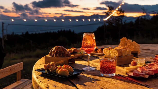 A wooden table set with food and drinks, overlooking a sunset with string lights in the background. - Hotel Monte Campo Ristorante Santa Lucia (Capracotta)