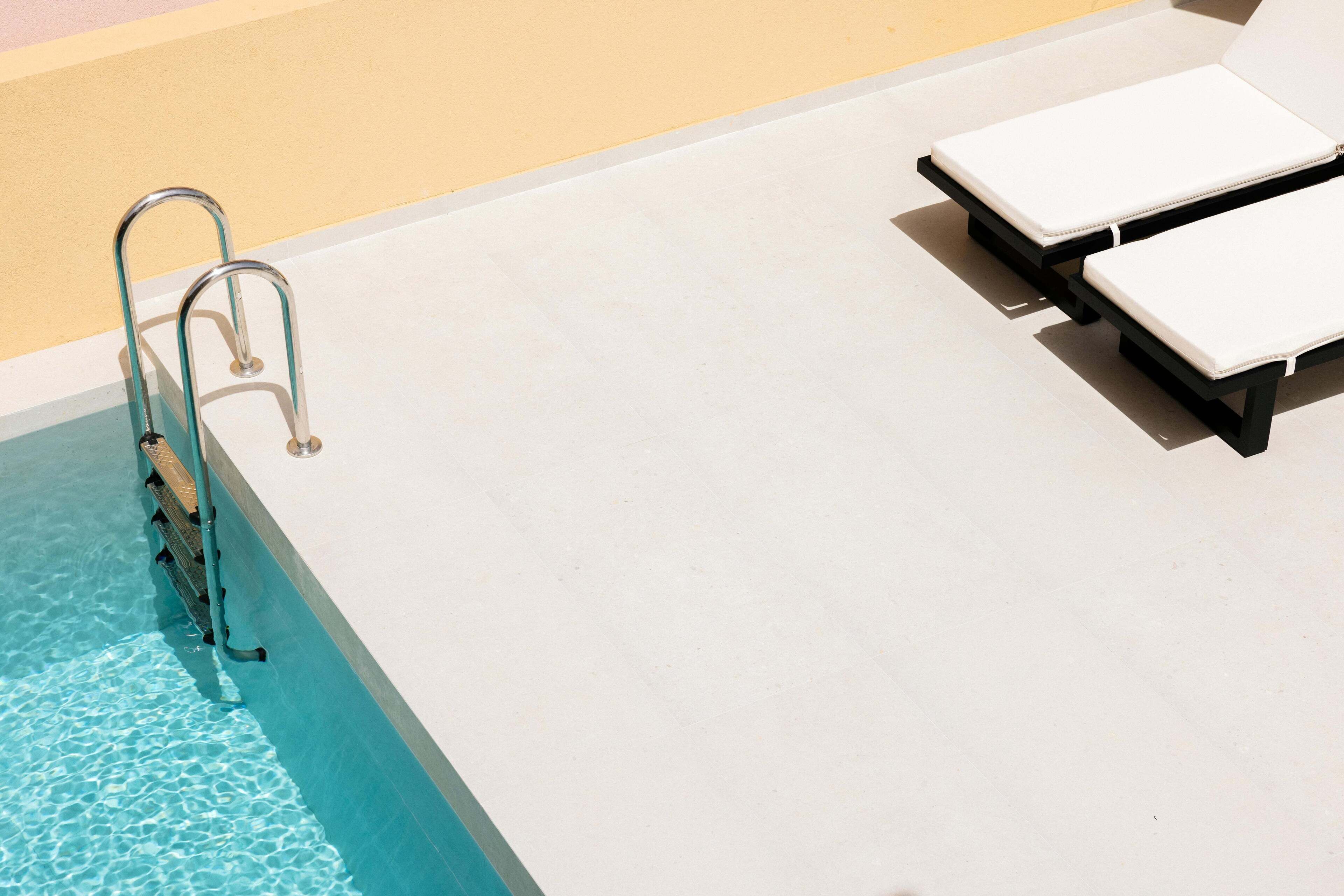 A swimming pool with a metal ladder and two lounge chairs.
