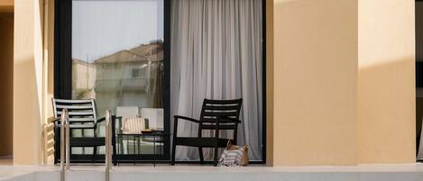 A pool area with two chairs and a table, a sliding glass door, and a view of a building in the background.