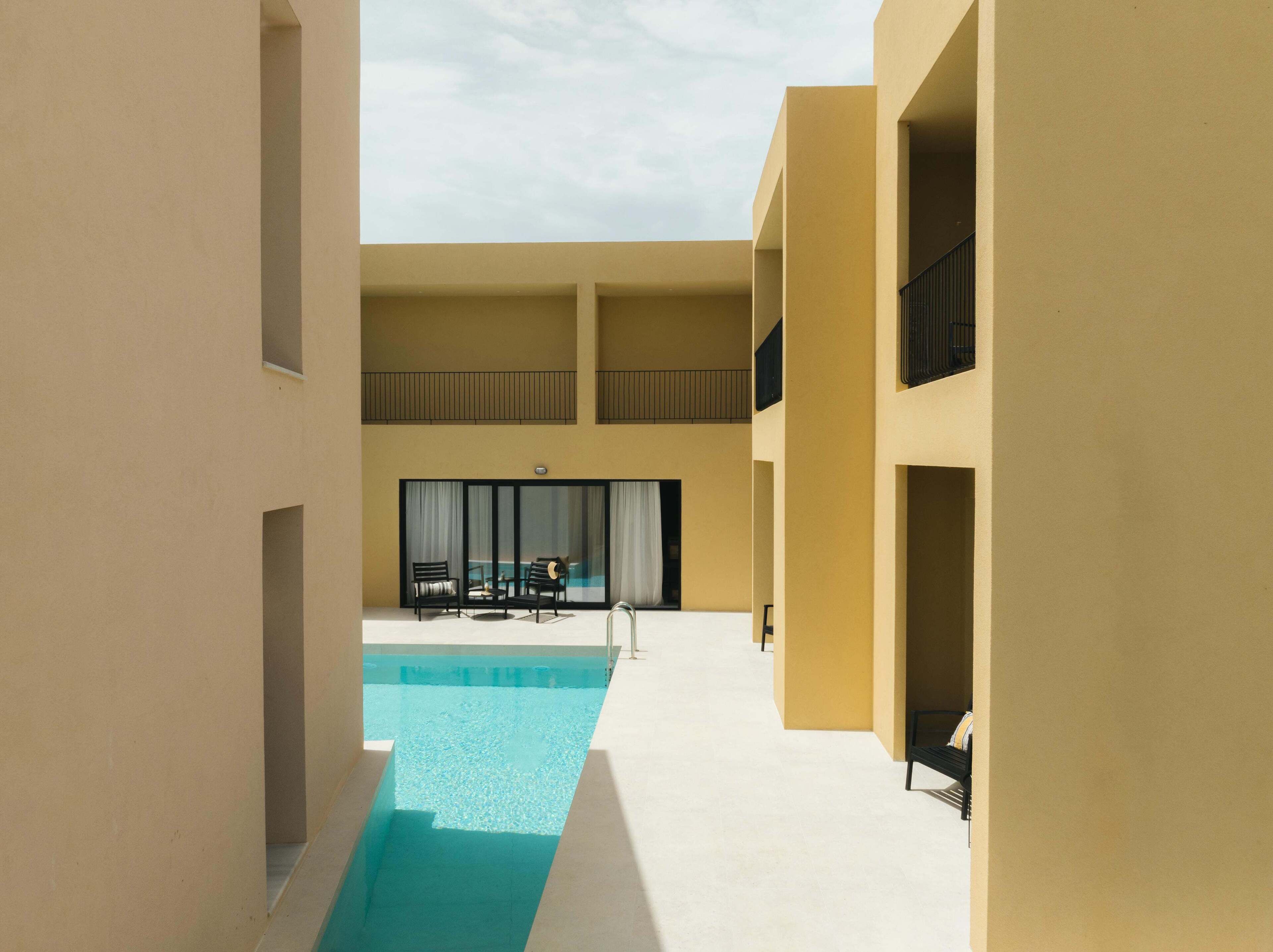 A modern building with a pool area, including a seating area with chairs and a table, and a view of a pool.