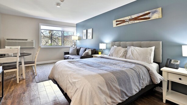 Een slaapkamer met een groot bed, een nachtkastje, een stoel, een raam en een airconditioning.
