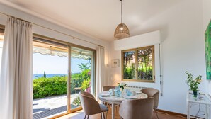 A dining area with a table, chairs, and a view of the sea through large sliding glass doors. - VILLA LA PETITE RESERVE VI4416 By Riviera Holiday (Eze)