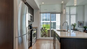 Une cuisine moderne dotée d’appareils électroménagers en acier inoxydable, d’un grand îlot central avec un évier et donnant sur un balcon.