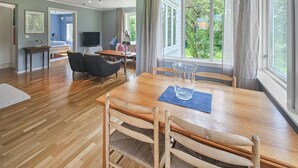 Un salon spacieux avec une table à manger en bois, deux chaises, un téléviseur et une grande fenêtre avec des rideaux.