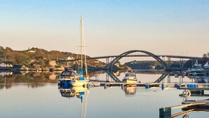 Un port de plaisance avec des bateaux amarrés, un pont en arrière-plan et une eau calme qui reflète le paysage.