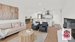 Ein modernes Wohnzimmer mit einer Couch, zwei Sesseln, einem Couchtisch und einer Küchenzeile mit Esstisch.