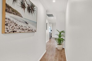 A hallway with a wooden floor, a potted plant, and a framed picture on the wall.