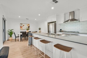A modern kitchen with a central island, bar stools, a refrigerator, and a stove.