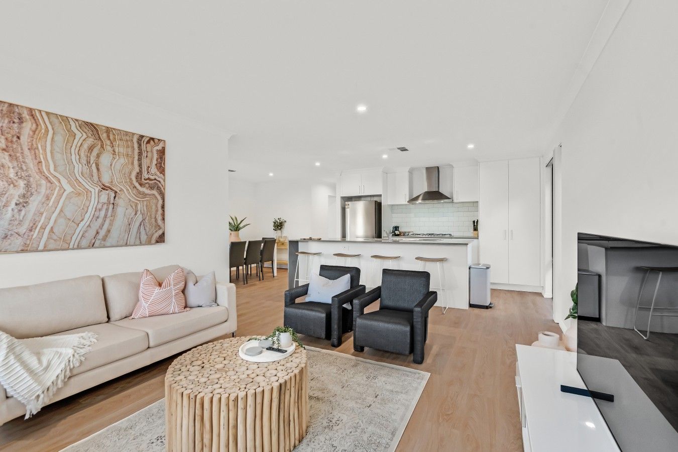 A modern living room with a sofa, coffee table, and two armchairs. A kitchen with a stove and cabinets is visible in the background.