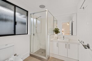 A modern bathroom with a glass-enclosed shower, a white sink, and a mirror above it.