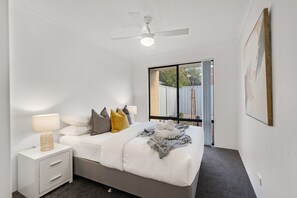 A bedroom with a bed, bedside tables, a ceiling fan, and a window with a view.