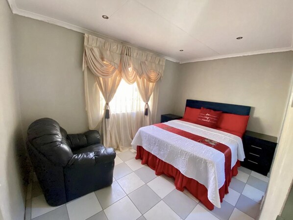 A bedroom with a bed, a chair, and a nightstand. - Newlands Comfortable Abode in Johannesburg (Johannesburg)