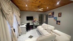 Una sala de estar moderna con techo de madera, un sofá blanco, un escritorio y un televisor.