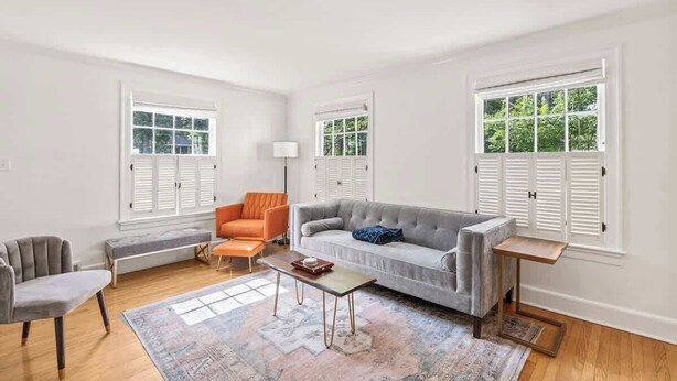 En stue med en grå sofa, en orange lænestol, en anden grå lænestol, et træbord og en bænk.