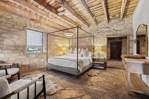 Une chambre aux murs de pierre, dotée d’un lit à baldaquin, d’une commode en bois et d’une fenêtre avec des stores.