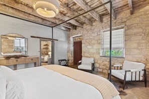 Une chambre avec un grand lit, des murs en pierre, un plafond en bois et un miroir.