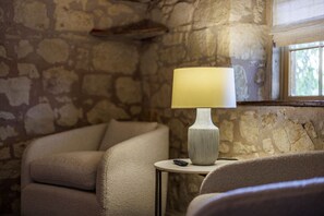 Een kamer met stenen muren, een ronde tafel, een lamp en een stoel.