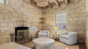 Une pièce rustique aux murs de pierre, dotée d’une cheminée, de deux fauteuils, d’une table ronde et d’un luminaire suspendu au plafond, fait de matériaux tressés.