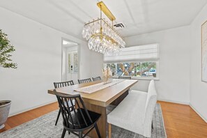 Een eetgedeelte met een houten tafel, zwarte stoelen, een kroonluchter en uitzicht door een raam.