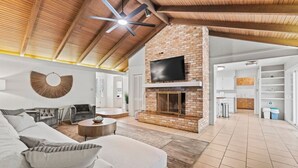 Amplia sala de estar con chimenea, televisor grande montado en una pared de ladrillo y ventilador de techo.