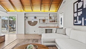 Una sala de estar moderna con un sofá blanco, una mesa de centro de madera y un comedor con un armario y estanterías blancas.