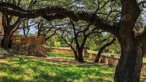 Un parque con una escalera de madera que conduce a una estructura de piedra, rodeado de árboles grandes y un sendero de tierra.