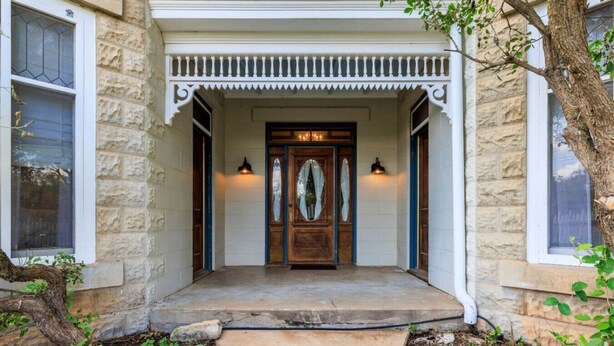 A stone house with a wooden front door, two windows, and a porch with a railing. - Danz Haus | Historic Home | Baron's Creek (Fredericksburg)