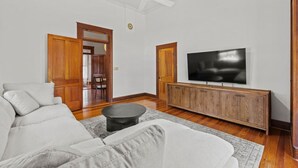 A living room with a white sofa, a wooden TV stand, a ceiling fan, and a wooden door. - Danz Haus | Historic Home | Baron's Creek (Fredericksburg)