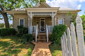 A two-story stone house with a porch, a front door, and a small staircase leading to the entrance.